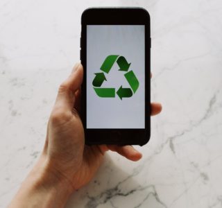 From above view of faceless person holding mobile phone with white screen and green recycle logo above marble surface