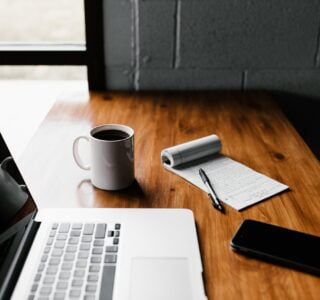 MacBook Pro, white ceramic mug,and black smartphone on table