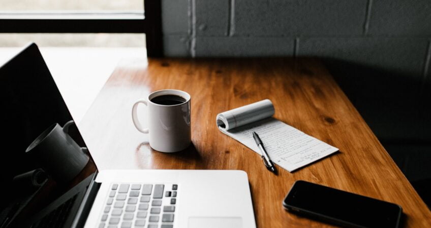 MacBook Pro, white ceramic mug,and black smartphone on table