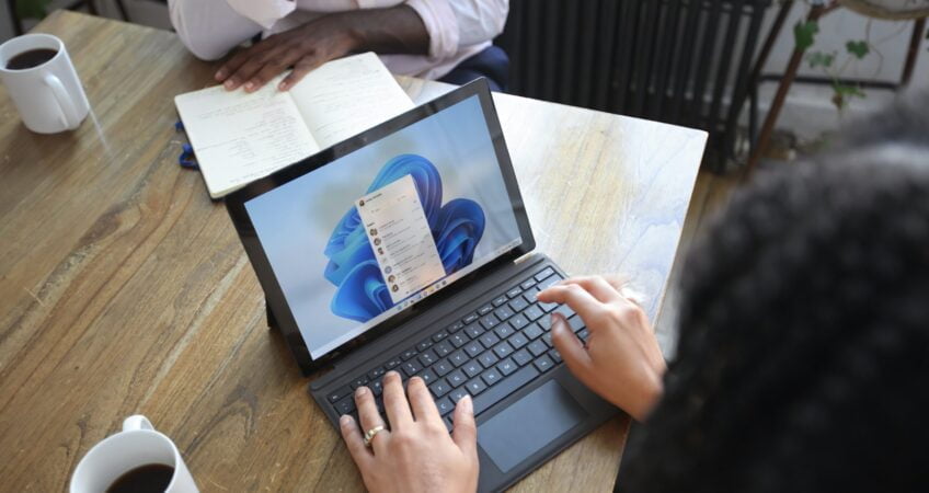 Overhead view of two people at a table working with a Microsoft laptop and notebook