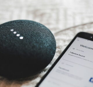 turned-on charcoal Google Home Mini and smartphone