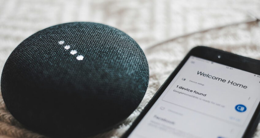 turned-on charcoal Google Home Mini and smartphone