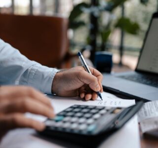 Free A person calculating finances with a calculator and pen on a desk indoors. Stock Photo