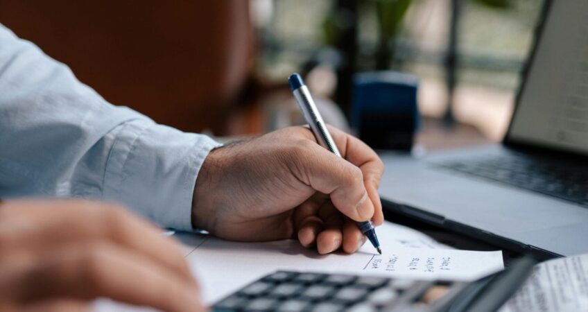 Free A person calculating finances with a calculator and pen on a desk indoors. Stock Photo
