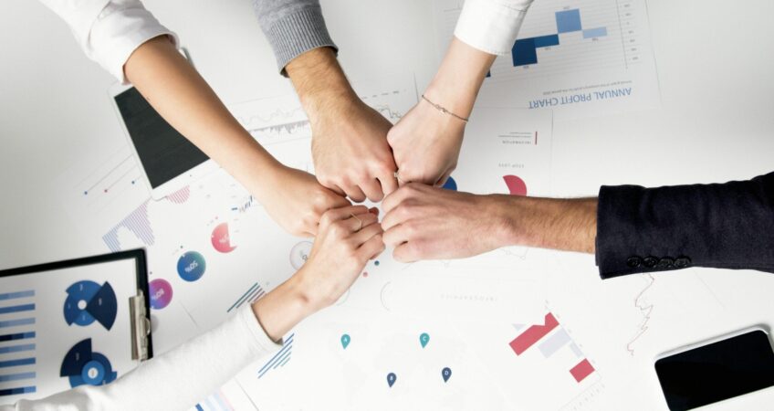 Free Colleagues celebrate success with a fist bump over financial charts depicting teamwork and unity. Stock Photo