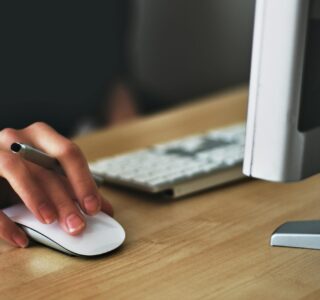 Free A hand using a wireless mouse at a modern desk setup with a computer and keyboard. Stock Photo