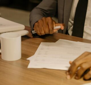 Free Close-up of a businessman holding and reviewing documents on a wooden desk. Stock Photo