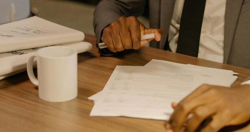 Free Close-up of a businessman holding and reviewing documents on a wooden desk. Stock Photo