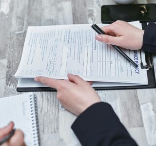 Free Close-up of hands analyzing insurance policy paperwork with pen on table. Stock Photo
