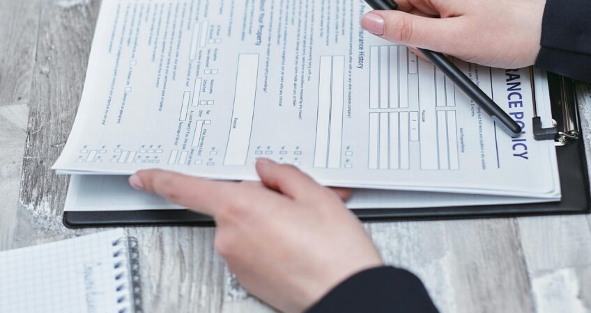 Free Close-up of hands analyzing insurance policy paperwork with pen on table. Stock Photo